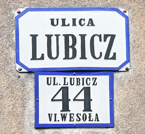 Fot. 29. W roku 1881 Rada Miasta Krakowa, utrzymując dotychczasowy podział na 8 dzielnic katastralnych (jedynie Dzielnicę I w miejsce nazwy „Kraków” nazwano „Śródmieściem”), wprowadziła nowe zasady ponumerowania orientacyjnego domów w mieście. Zasady te przetrwały do dzisiaj: numeracja domów ulicami (a nie dzielnicami katastralnymi, jak poprzednio), początek numerowania od strony bliższej Rynkowi Głównemu (na Stradomiu bliższej ul. Stradomskiej, na Kazimierzu bliższej ul. Krakowskiej), numery nieparzyste po prawej stronie. Wprowadzono jednolite dla całego miasta kolory tabliczek z nazwami ulic i tabliczek orientacyjnych z numerami domów: litery i cyfry koloru czarnego, tło białe, obwódki tablic niebieskie (DzRMK 1881, nr 1, s. 2–3). Przydzielone wówczas nowe numery domów pozostały już z reguły niezmienione do naszych czasów (zmiany w przynależności dzielnicowej ulic nie miały znaczenia dla numeru domu), natomiast sam wzór tabliczek wprawdzie był aktualny jeszcze w okresie okupacji, jednak już w okresie międzywojennym podlegał wymianie na znany nam co do kolorystyki z codzienności wzór nowy, z białymi literami i cyframi na niebieskim tle, z białą obwódką. Powyżej: 3) zaprezentowane obok tabliczki z domu przy ul. Lubicz (dziś postarzałe i pociemniałe) zgodnie z wytycznymi z roku 1881 pierwotnie wyglądały inaczej – na zdjęciu zrekonstruowano ówczesną kolorystykę.